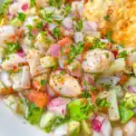 A close-up of fresh ceviche featuring diced fish, avocado, tomatoes, red onion, cucumber, and herbs, all mixed with spices and garnished with chopped parsley.