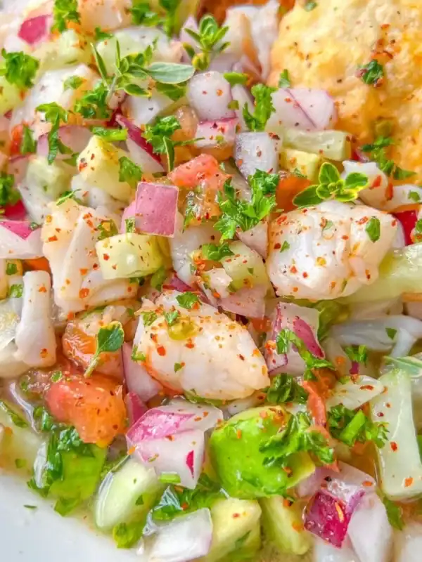 A close-up of fresh ceviche featuring diced fish, avocado, tomatoes, red onion, cucumber, and herbs, all mixed with spices and garnished with chopped parsley.