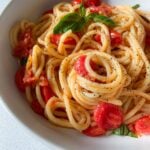 A bowl of Cherry Tomato Pasta with fresh basil and a sprinkle of black pepper, served in a white dish on a light surface.