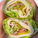 Two hands hold a lettuce wrap sliced in half, revealing layers of turkey, cheese, pickles, onions, and more crisp lettuce rolled tightly inside—no bread in sight for this fresh Lettuce Wrap delight.