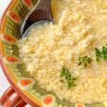 A bowl of Stracciatella Soup with small pasta, garnished with fresh herbs. The bowl features a colorful patterned rim, and a wooden spoon rests inside the comforting soup.