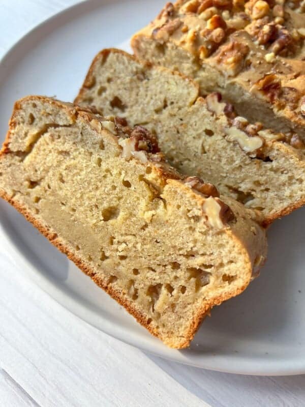 Sliced loaf of banana bread with chopped walnuts on top, displayed on a white plate. The bread is golden brown, showcasing a moist and fluffy texture.