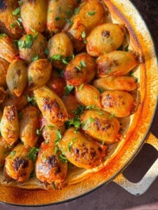 A close-up of a baked dish featuring caramelized onions garnished with fresh parsley. The onions are golden brown and neatly arranged in a circular, rustic baking dish. Sunlight highlights the vibrant colors and crispy texture of the onions.