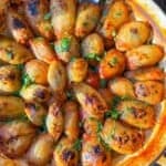 A top view of a baked dish featuring golden-brown stuffed onions, sprinkled with fresh herbs. The onions are arranged in a circular pattern, placed in a round baking dish, with a serving spoon resting at the edge.