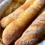 Three crispy, golden baguettes rest on parchment paper in a white, fluted baking dish.