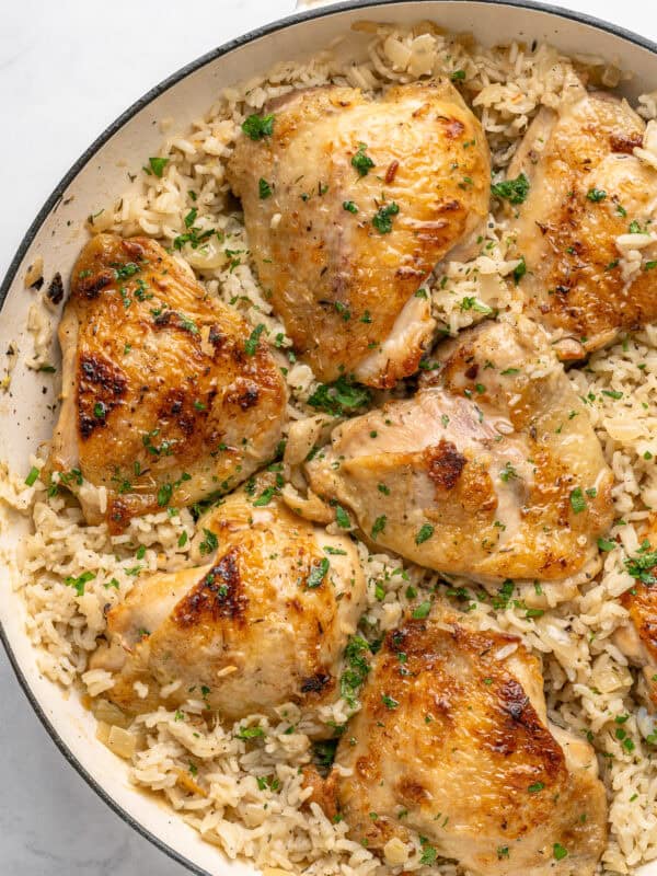 Golden-brown chicken thighs on a bed of seasoned rice, garnished with chopped parsley and inspired by the bold flavors of Mexican Hot Dogs, served in a white skillet.