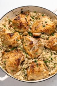 A white pan filled with golden-brown cooked chicken thighs on top of a bed of rice, garnished with chopped parsley—an inviting dish perfect alongside Mexican Hot Dogs for a flavorful meal.