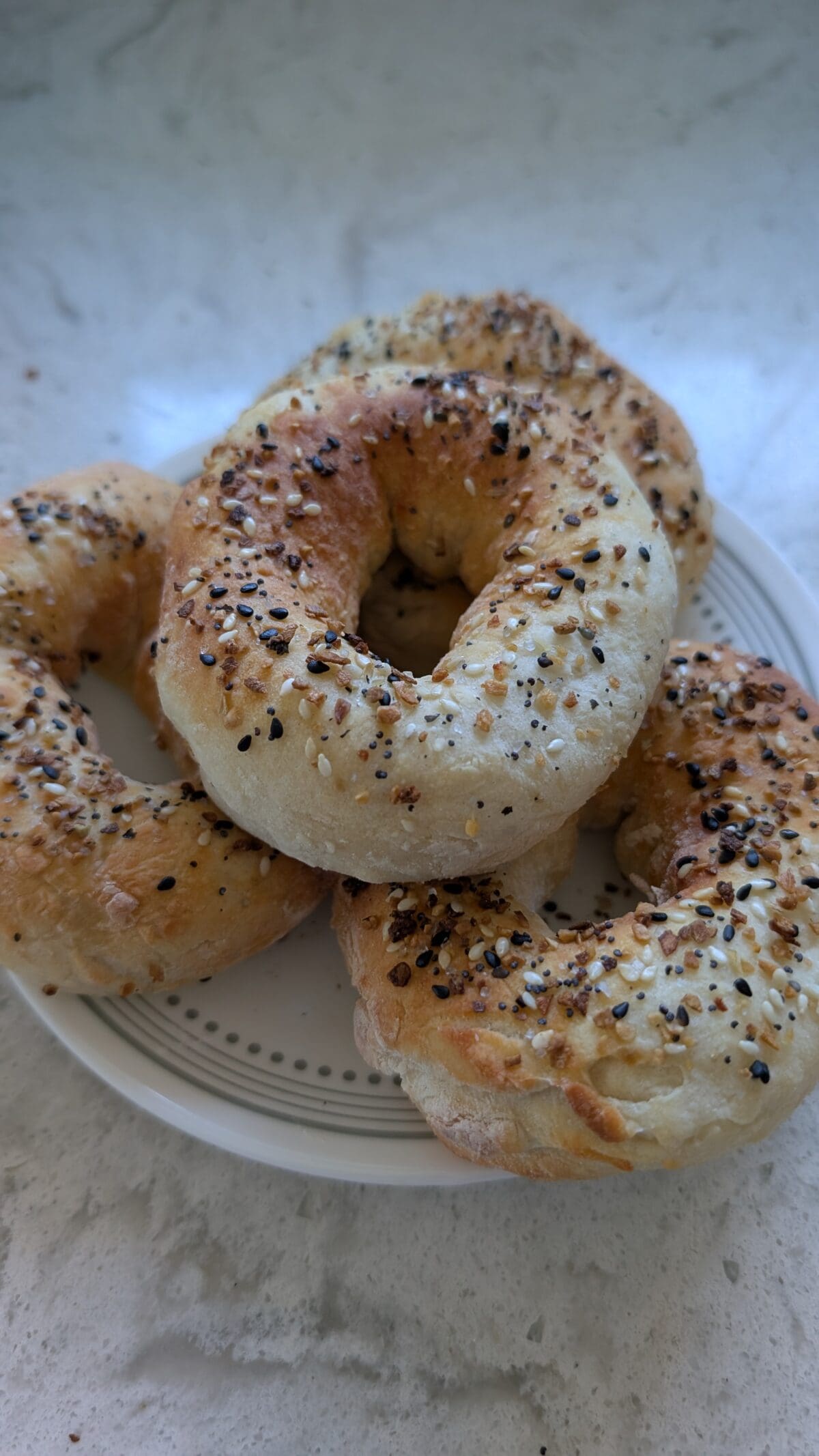 A plate of homemade Cottage Cheese Bagels topped with sesame seeds, poppy seeds, and seasoning, set on a light-colored countertop.