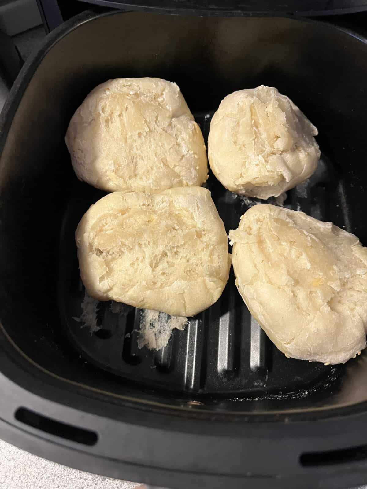 Four pieces of uncooked dough are placed inside the basket of an air fryer, ready to be baked or cooked.