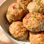 A bowl of golden-brown meatballs garnished with chopped parsley. The meatballs are visibly seasoned with herbs and spices, adding color and texture to the dish. Sunlight enhances the dish's appetizing appearance.