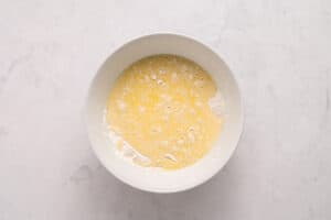 A white bowl on a light marble surface, containing a mixture of flour and beaten eggs, partially blended together.