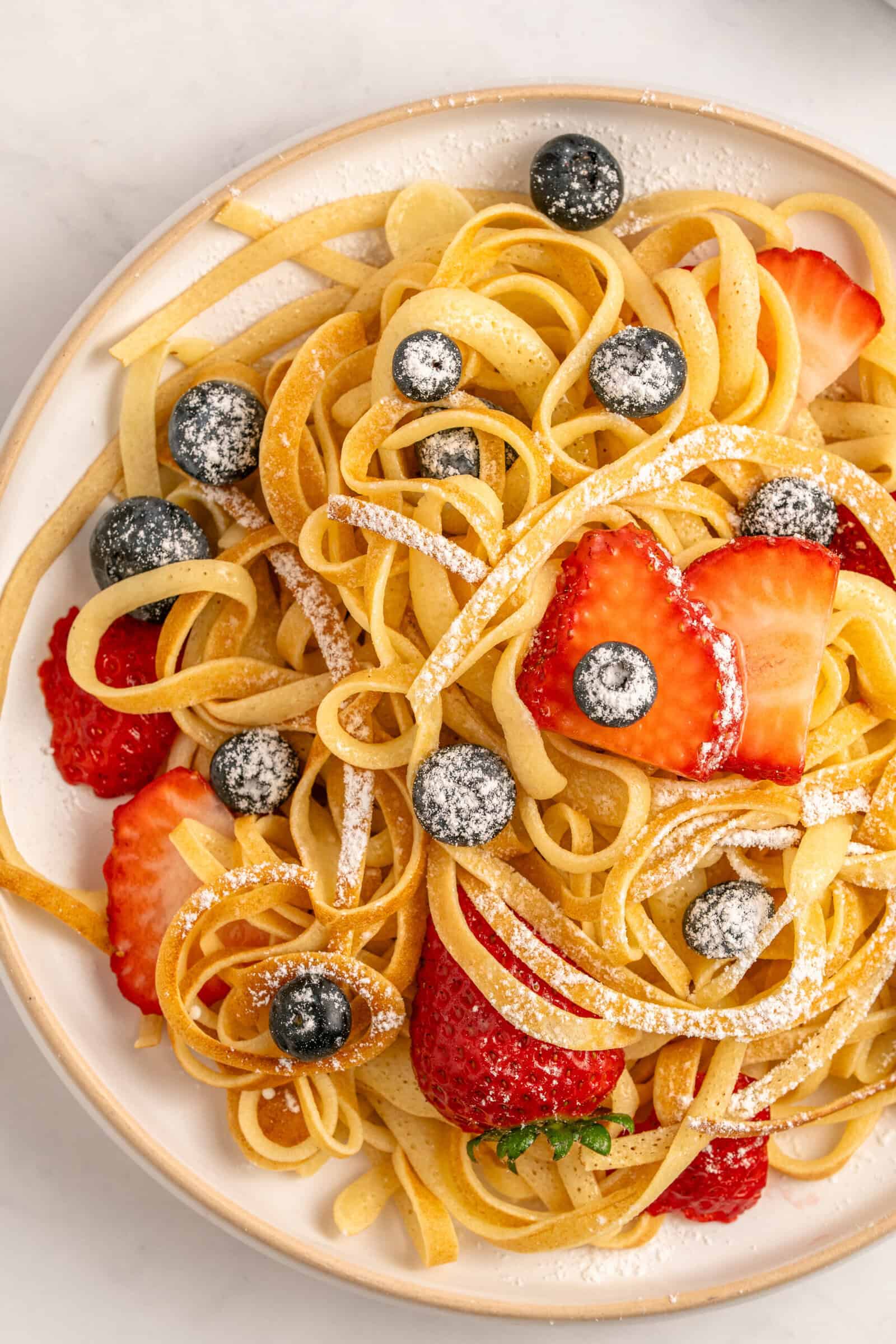Photo of pancake spaghetti with berries and powdered sugar on top. 