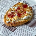 A slice of toast topped with cottage cheese, peanut butter, and strawberry jelly sits on a plate designed to look like a newspaper page.