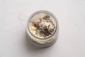 A glass jar filled with milk, chia seeds, a scoop of protein powder, and a dollop of peanut butter on a light, smooth surface.
