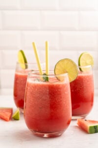 A group of glasses with watermelon juice and lime slices.
