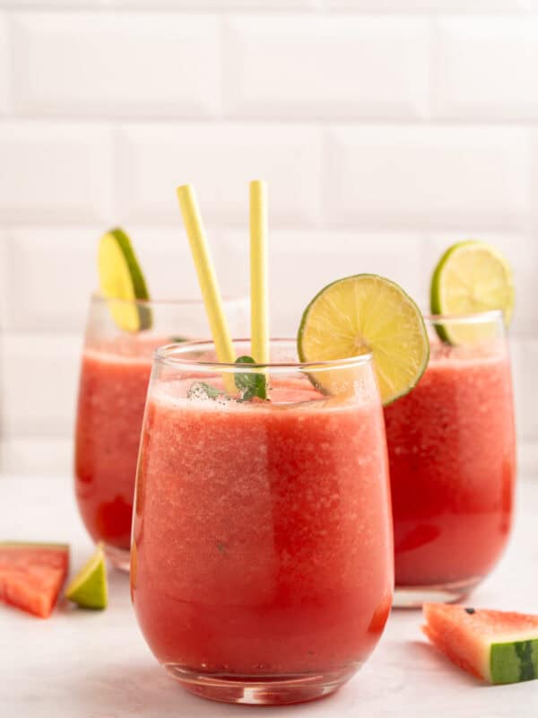 A group of glasses with watermelon juice and lime slices.
