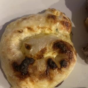 A close-up of a Rice Paper Burek pastry with a golden-brown, bubbly, and slightly charred cheesy topping on a white plate.