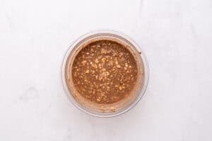 A glass bowl filled with a mixture of oats and chocolate liquid sits on a light marble surface.