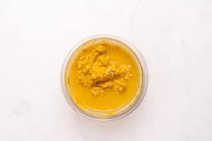 A glass bowl filled with chunky, golden-yellow liquid, possibly a curry or sauce, placed on a white marble surface.