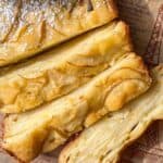 Close-up of several slices of a golden, layered Invisible Pear Cake with thin apple slices visible throughout. The cake is dusted with powdered sugar and placed on a sheet of printed parchment paper.