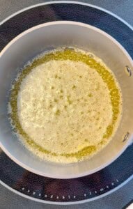 A close-up view of a saucepan on a stovetop, with melted butter bubbling and foaming around the edges.