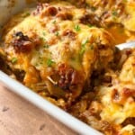 Close-up of a baked Cabbage Lasagna in a white dish, featuring a golden, melted cheese topping with browned edges and sprinkled with fresh chopped herbs. A serving spoon is lifting a portion from the dish.