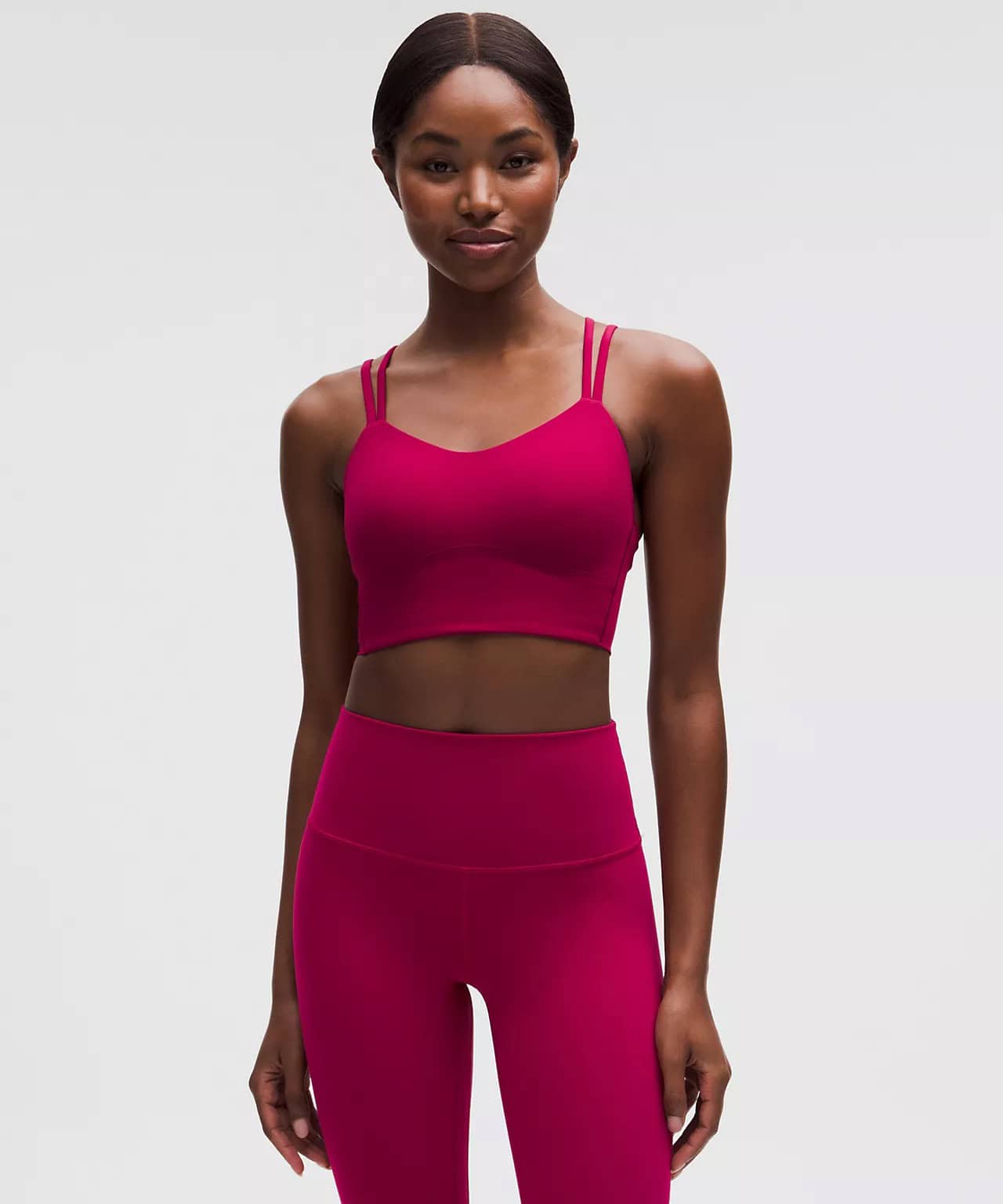 A woman stands facing forward, wearing a matching magenta sports bra with double shoulder straps and high-waisted leggings, against a plain light gray backgroundโperfect for those seeking exclusive deals on stylish activewear.