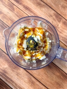 A food processor bowl with ricotta cheese, zest, and honey sits on a wooden surface—perfect for pairing with honey glazed carrots.