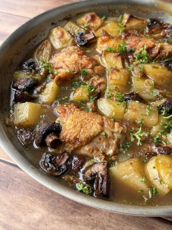 A skillet filled with golden-brown, crispy chicken thighs, potatoes, mushrooms, and fresh herbs in a savory broth, all cooked together and garnished with chopped parsley—a delicious crispy chicken thighs recipe.