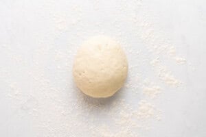 A ball of dough sits on a white surface lightly dusted with flour.