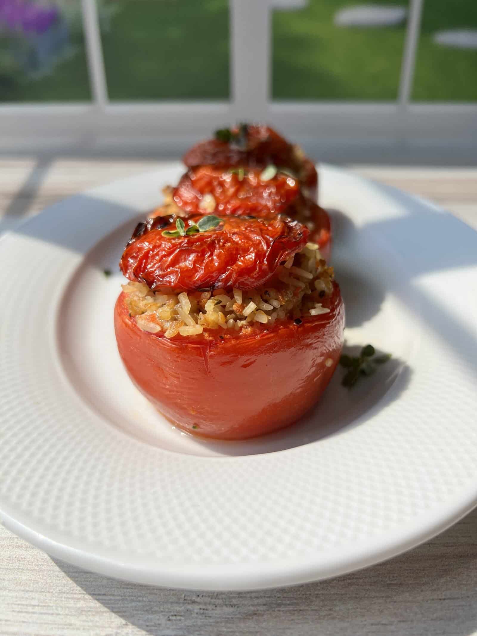 Three stuffed tomatoes filled with rice and herbs, topped with roasted tomato slices and garnished with fresh thyme, served on a white plate with sunlight streaming through a window in the background. - 4