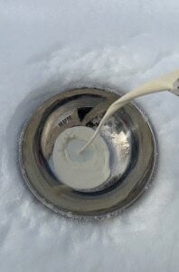 A stream of cream is being poured into a metal bowl placed on snow, with the cream beginning to pool in the center—perfect for making Viral Snow Ice Cream.