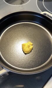 A small dollop of yellow butter or ghee sits in the center of a black, empty cast iron skillet on a stovetop, ready to be melted for cooking a High Protein Dutch Baby.