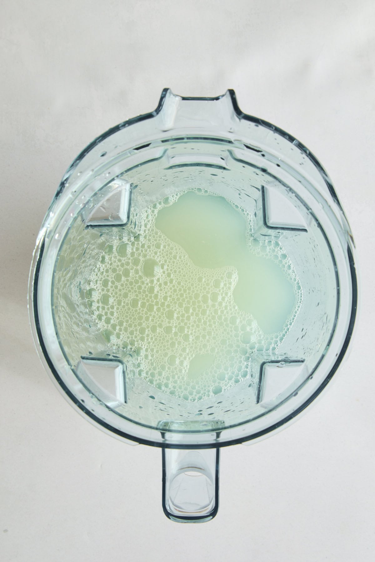 Top view of a blender containing a pale, frothy liquid with bubbles, set against a white background.