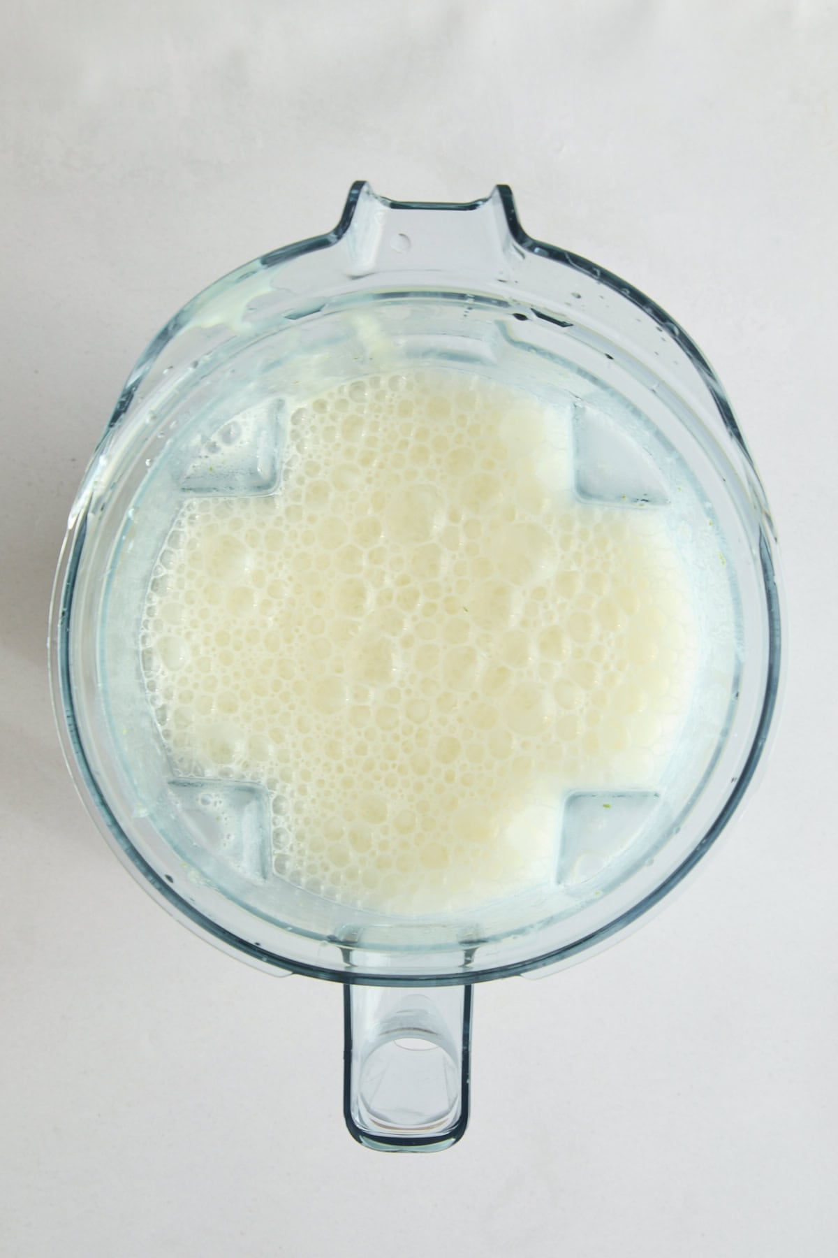 A top-down view of a blender filled with Brazilian Lemonade - a frothy, blended milk or a milk-based liquid against a light background.