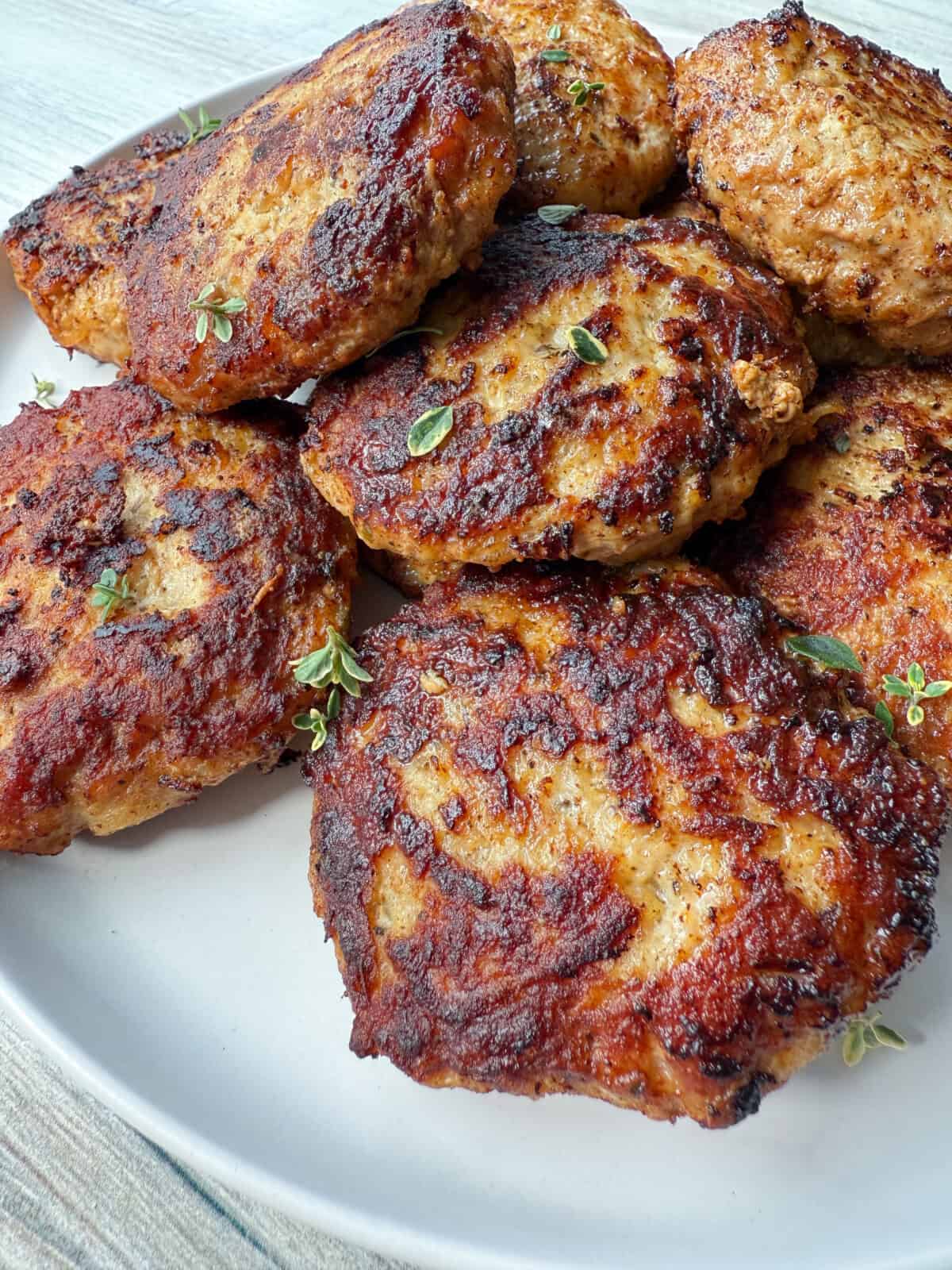A plate of browned, grilled chicken patties garnished with small sprigs of fresh herbs, displayed on a white plate.