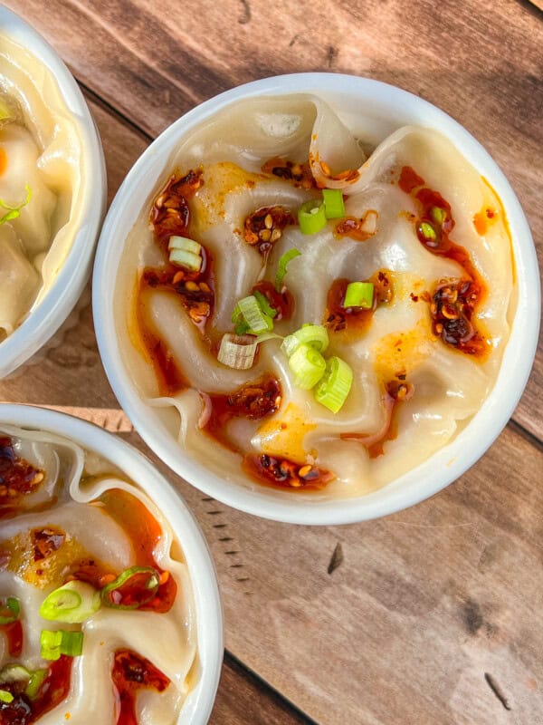 A bowl of dumplings topped with chili oil and chopped green onions, placed on a wooden surface. - 6