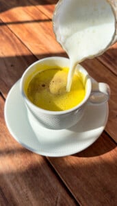 A white cup with yellow liquid, reminiscent of viral egg coffee, and a spoon being poured into it.