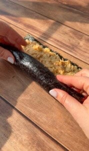 Close-up of hands rolling sushi with a bamboo mat, nori seaweed, and a rice filling on a wooden surface.