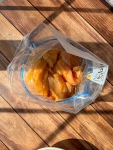 Healthy Chicken Tenders marinating in a clear plastic ziplock bag, placed on a wooden surface with sunlight and shadows falling across the scene.