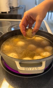 A person holding a ball of meatball in a pot of broth.