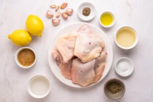 A plate of raw chicken with spices and lemons.