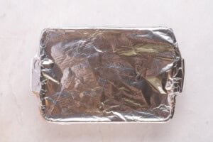 A rectangular baking dish covered tightly with aluminum foil, placed on a light-colored marble surface.