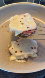 A spatula lifts a cooked patty topped with melted Swiss cheese and ham from a frying pan, while another similar patty is still cooking—perfect for enjoying with low carb mortadella wraps.