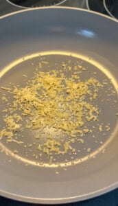 parmesan sizzling in a light gray nonstick pan, beginning to cook with a few drops of oil visible—the perfect aromatic base for making delicious Low Carb Mortadella Wraps.