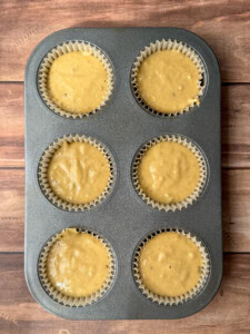 A six-cup muffin tray lined with paper cups, each filled with healthy sweet potato muffins batter, sits on a wooden surface, ready to be baked.