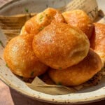 A ceramic bowl lined with parchment paper holds several golden-brown Air Fryer Parmesan Cheese Balls, sprinkled with herbs, and bathed in warm sunlight.