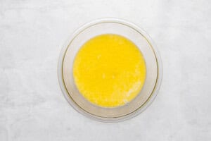 A glass bowl filled with melted butter sits on a white marble surface.
