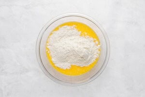 A glass bowl containing melted butter and a mound of flour sits on a white marble surface, ready for mixing.
