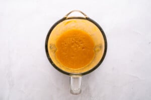 Top view of a glass measuring cup filled with a smooth, orange-yellow blended mixture, placed on a light, textured surface.